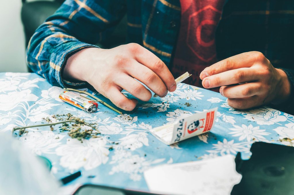 A close-up of a man rolling a joint with marijuana and rolling papers on a table.